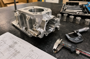 Aluminum 6061 automotive prototype with precision CNC-machined surfaces, engineering drawings, and inspection tools on a manufacturing workbench.