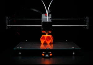 Close-up of an FDM 3D printer producing an orange prototype part directly from a CAD design. The image illustrates rapid prototyping for product development, enabling engineers to quickly test, refine, and validate designs before investing in production tooling or mass manufacturing.