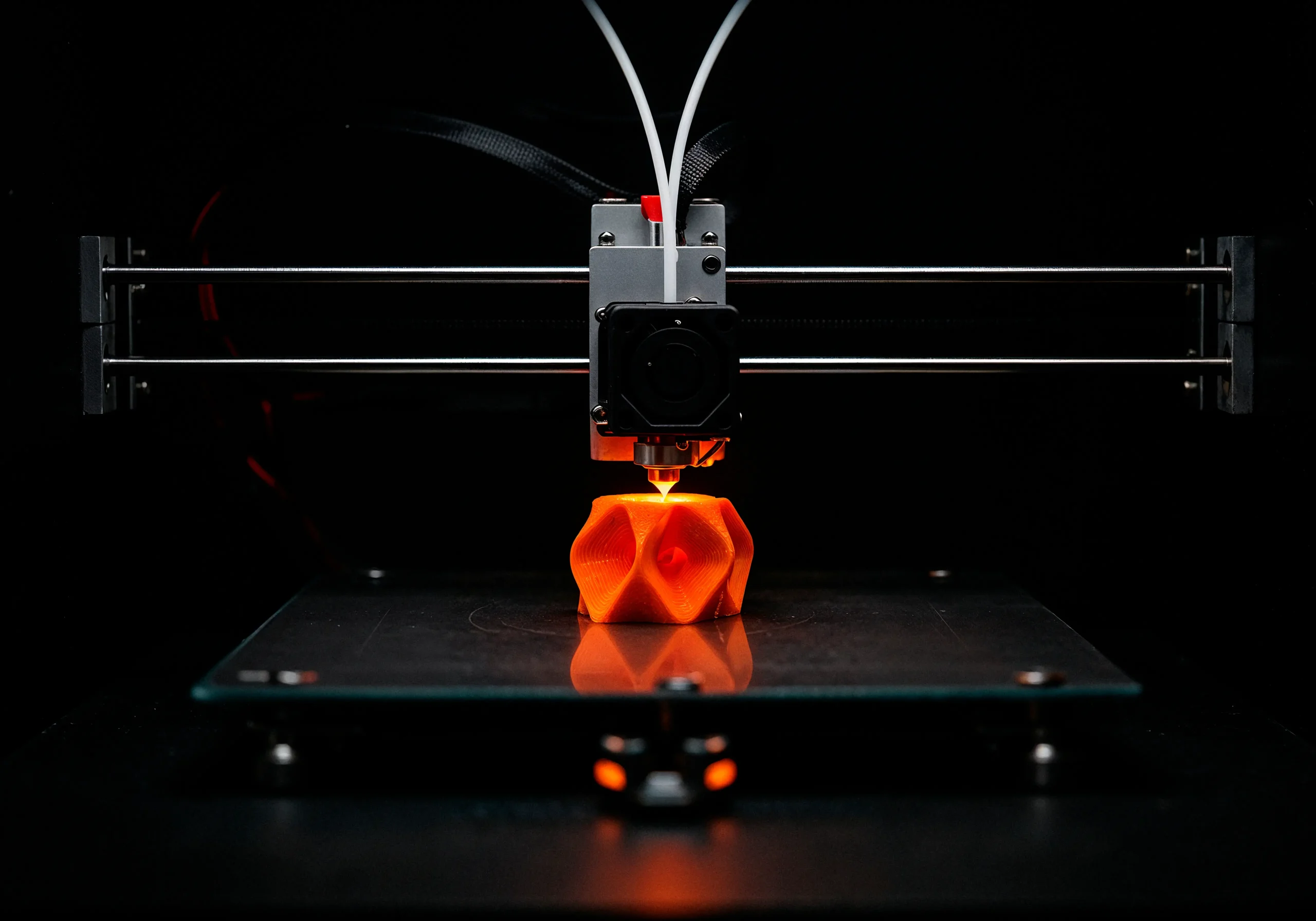 Close-up of an FDM 3D printer producing an orange prototype part directly from a CAD design. The image illustrates rapid prototyping for product development, enabling engineers to quickly test, refine, and validate designs before investing in production tooling or mass manufacturing.